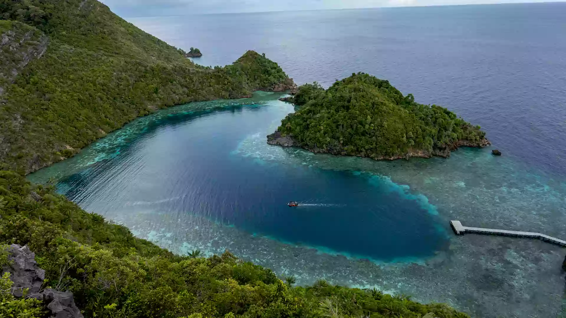 Pulau Karawapop dengan laguna biru tenang dan dermaga kecil, dikelilingi bukit hijau alami.